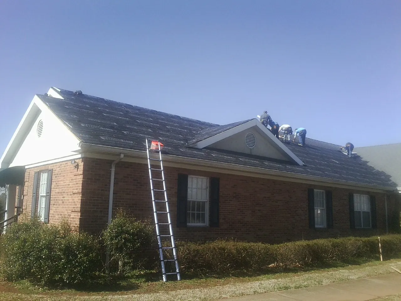 Crew tearing shingles off a brick ranch roof with a ladder set — Emergency Roof Repair work by our crew in Intercourse