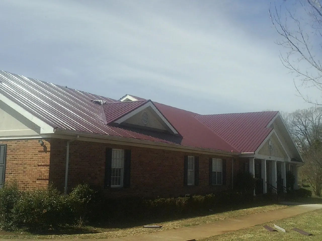 Red metal roof with gabled entries on a long brick building, from a Hail Damage Roof Repair job in Intercourse