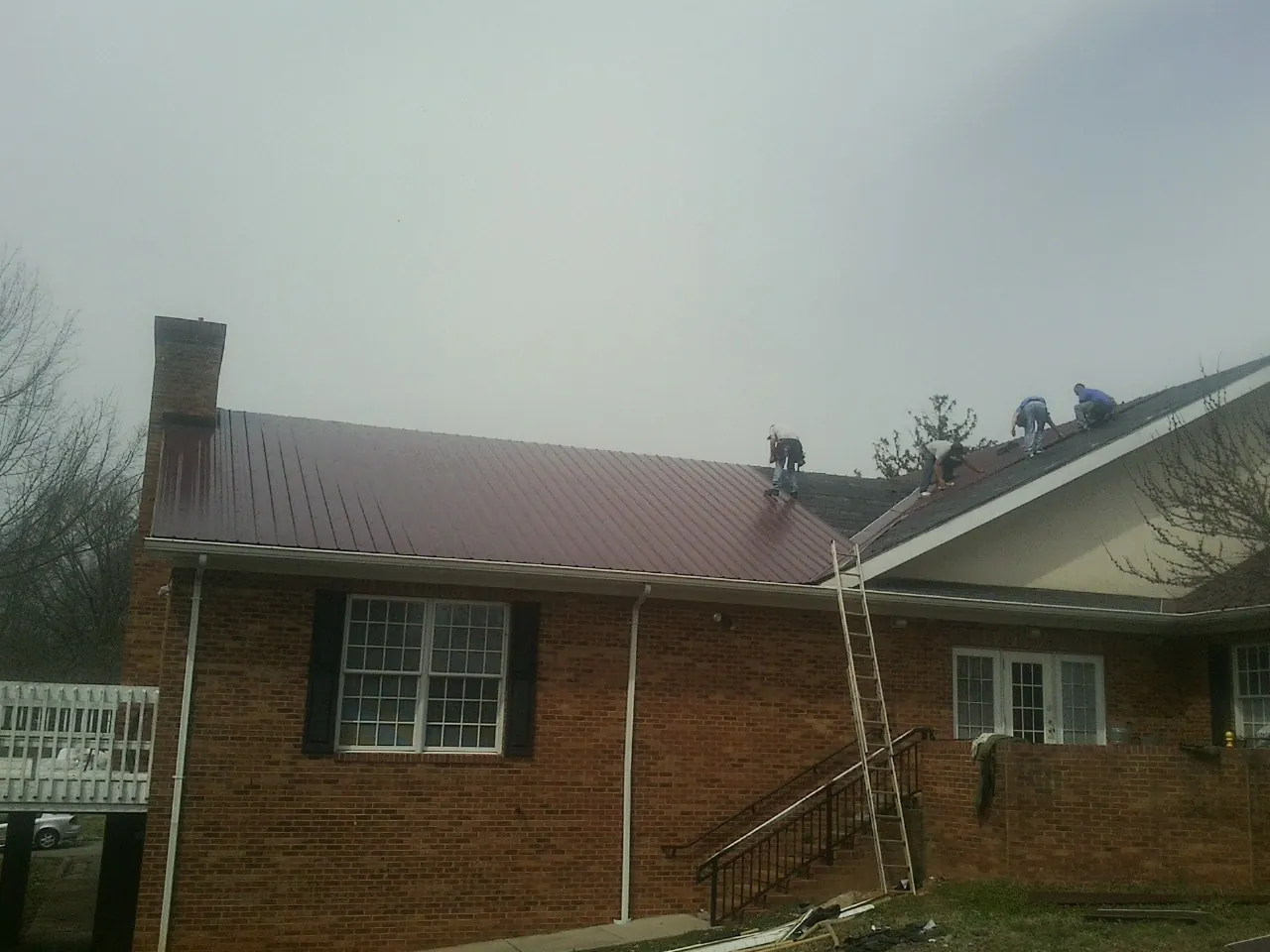 Crew setting red metal roofing panels on a brick home in Intercourse