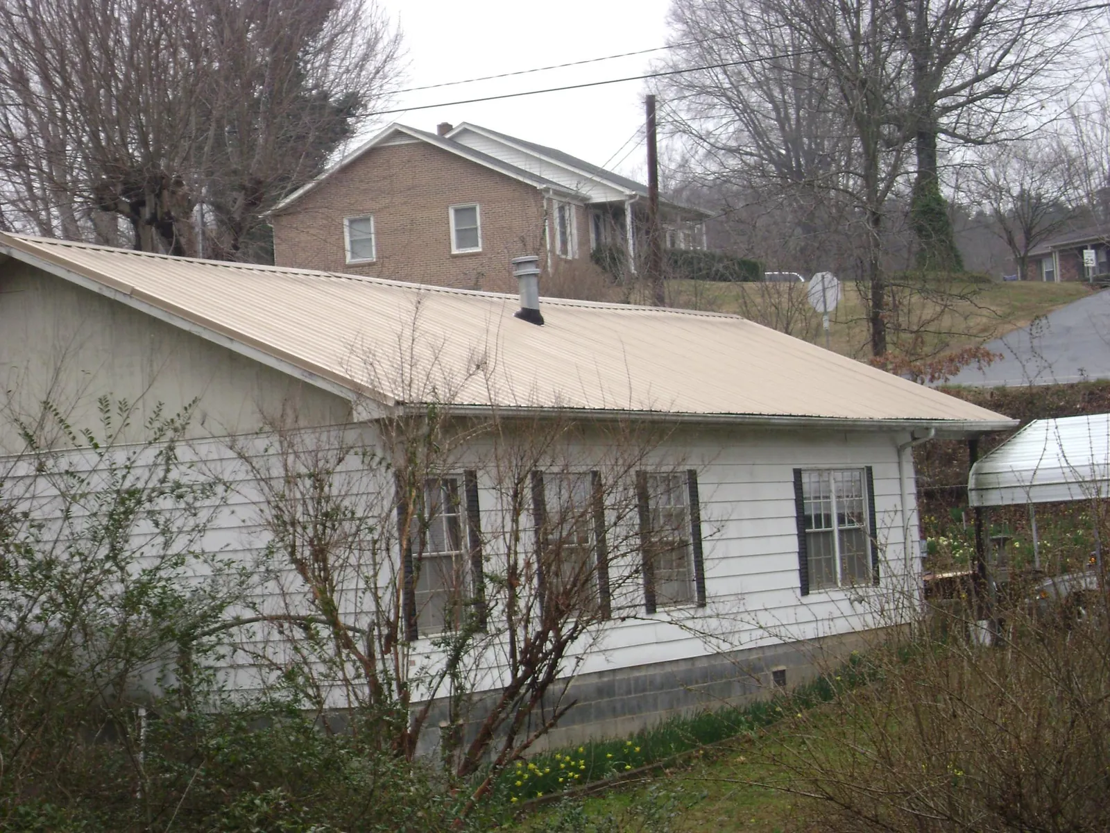 Tan metal roof on a white sided house set into a hillside — Commercial Roofing by Roofing Brothers in Intercourse